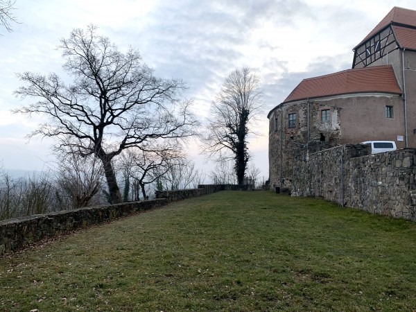 Trávník, vlevo zeď a svah, vpravo kamenná zeď domu