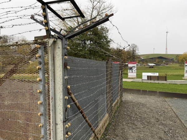 Roh hraničního plotu s betonovými sloupky. Plot je shora dopředu celý omotaný ostnatým drátem.