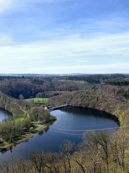 Přehrada v zalesněné krajině. Velký hrad vpravo.